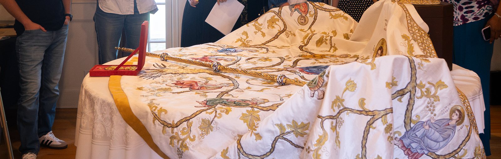 An embroidered white vestment with gold vines and icons, and a gold pastoral staff, laid out on a round table
